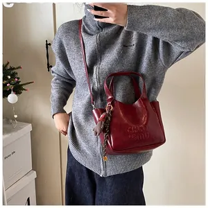 Detail of burgundy glossy tote bag with embossed text and bear charm accessory