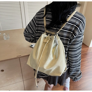 Detail of light yellow bucket bag featuring drawstring closure and metallic woven charm