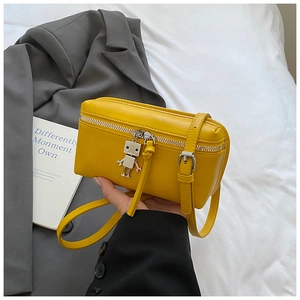 Detail of yellow leather mini box bag featuring a silver robot charm and adjustable buckle
