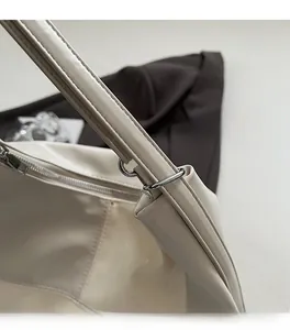 Détail macro du similicuir crème et de l'anneau métallique argenté poli sur le sac cabas