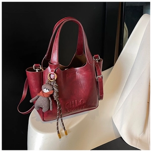 Detail of burgundy leather tote bag with embossed lettering and cute bear charm accessory