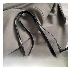 Detail der weißen Handtasche in Knitteroptik mit schwarzen glänzenden Lackledergriffen