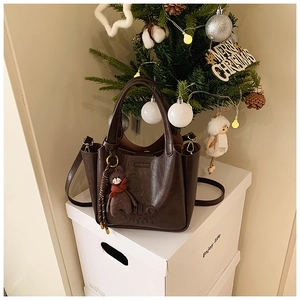 Detail of vintage brown leather handbag with debossed letters and a cute bear charm