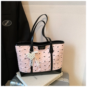 Detail of pink pleated tote bag with black bows and pearl heart charm on a suitcase