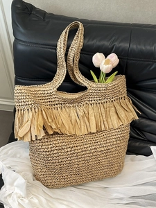Handwoven straw tote bag with fringe trim and tulips on a black leather background