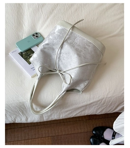 Close-up of a white bucket bag with butterfly embossing and drawstring bow detail