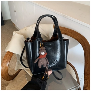 Detail of black leather tote bag with embossed letters and a cute plush bear charm