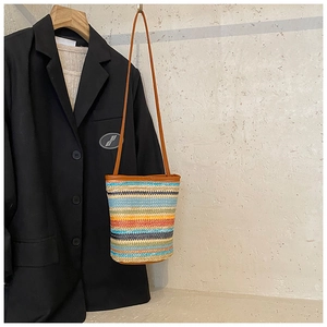 Close-up of a colorful striped woven straw bucket bag with a slim brown leather strap