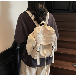 Vista posteriore di uno zaino minimalista in nylon beige indossato da una modella su scale