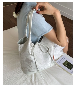 Detailed view of white bucket bag with silver butterfly patterns and drawstring closure