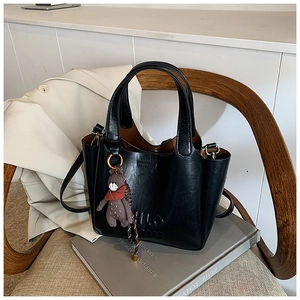Close-up of black bucket bag with HLO embossing and a cute brown bear charm