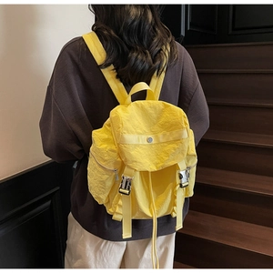 Detailed view of yellow nylon backpack with metallic buckles on textured crinkled fabric