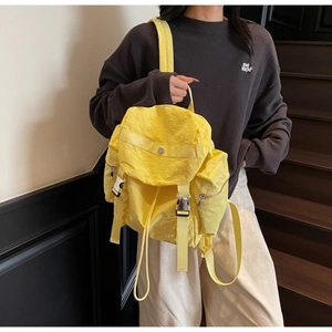 Detail of yellow nylon backpack with silver buckles worn by model on stairs