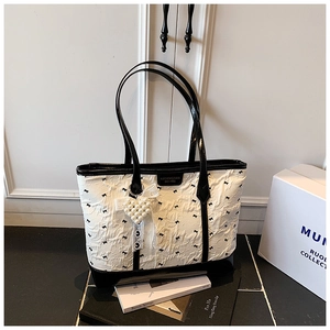 Detail einer weißen Shopper-Tasche mit Faltenstruktur und schwarzer Schleifenstickerei-Anhänger