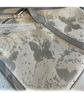 Dettaglio della borsa tote in raso argento con stampe a farfalla e borchie su pizzo
