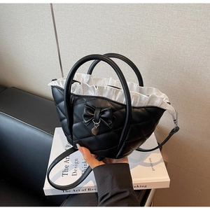 Detail of black quilted bucket bag featuring a bow, heart pendant, and ruffle lining