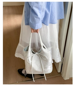 Detail shot of a white bucket bag with an elegant bow accent held by a model