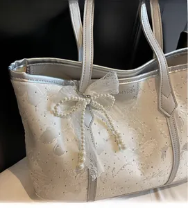 Dettaglio della borsa tote bianca ricamata con farfalle e ciondolo a fiocco di pizzo