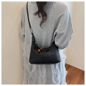 Detail of black polka dot crossbody bag with wooden bead charm on a grey sweater and white skirt