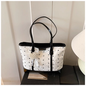Detail of white wrinkled tote bag featuring black bow prints and a heart pearl charm