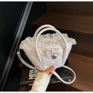 Close-up of white quilted bucket bag with bow detail and heart pendant on a book