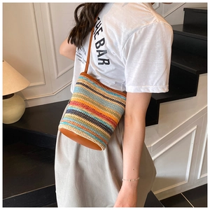 Detailed view of bohemian straw bucket bag with colorful stripes and leather base