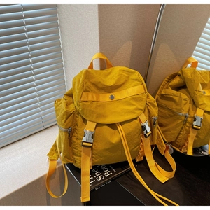 Dettaglio dello zaino in nylon giallo con fibbie metalliche e tasca laterale zip