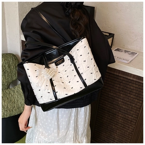 Detail of a monochrome tote bag featuring heart pearl charms and bow print texture