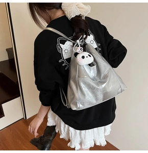 Détail d'un sac à dos argenté métallisé avec pendentif panda en peluche et cordon de serrage