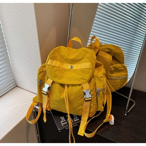 Dettaglio dello zaino in nylon giallo senape con patta a doppia fibbia e tasche laterali