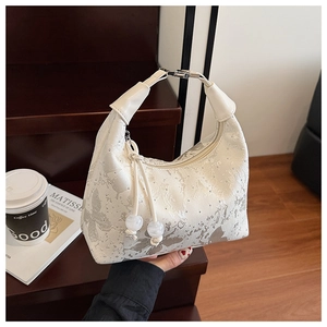 Close-up of a white hobo bag with silver floral patterns and tassel charm detail