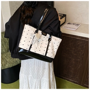 Detail of white wrinkled tote bag featuring black bow patterns and pearl cluster charm