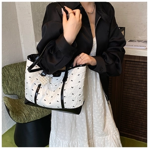 Detail of a white bow-print tote bag with black leather trim and pearl heart charm