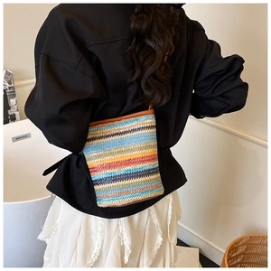 Detail of colorful striped straw crossbody bag with brown leather trim in a lifestyle view