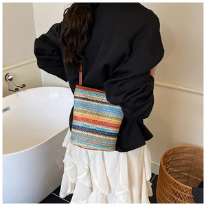 Detailed close-up of rainbow woven straw bucket bag with brown leather handle details