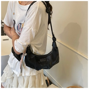 Detail of black crescent hobo bag featuring glossy nylon texture and silver heart pendant