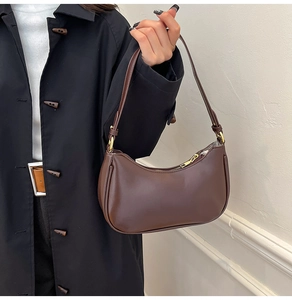 Detail of a deep brown half-moon underarm bag with gold zipper and smooth leather texture