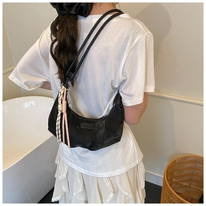 Detail of black crescent shoulder bag featuring a unique tricolor braided rope pendant