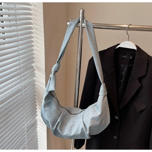 Detail of light grey crescent bag with knotted strap hanging in soft natural light