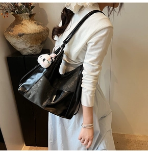 Détail d'un grand cabas en cuir verni noir avec charm ours sur un pull en tricot blanc