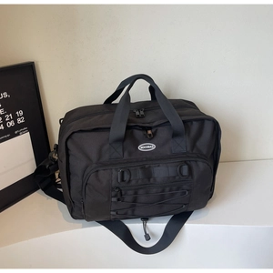 Detail of a large black nylon travel bag with crossbody strap and front bungee storage