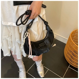 Close-up of black glossy dumpling bag with pleated texture and stylish side charms
