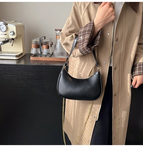 Close-up of a black leather crescent shoulder bag with golden chain detail and zipper