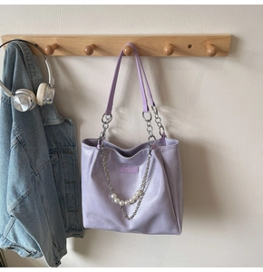 Detail of lavender tote bag with pearl chain hanging on a wooden rack in a home setting