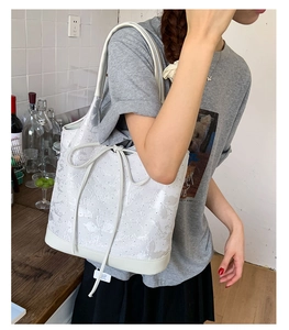 Detail view of a white tote bag with silver floral patterns and drawstring bow detail