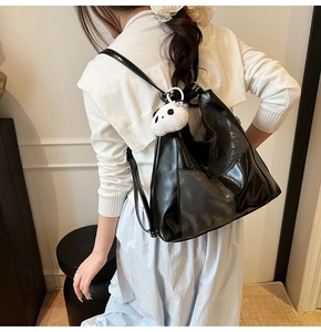 Détail d'un sac à dos en cuir noir brillant avec un joli charme panda sur la bandoulière