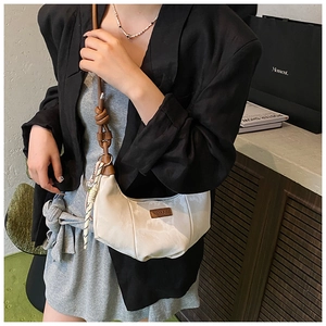 Detail view of cream dumpling bag featuring pleated fabric and brown leather knotted strap