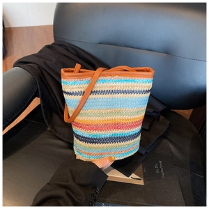 Detail of colorful woven straw bucket bag with brown leather trim on stylish black seat