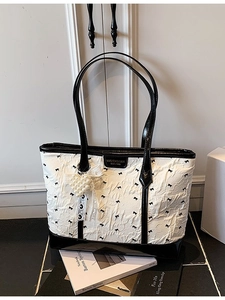 Chic white pleated tote bag with black bow print and pearl heart charm on marble stand
