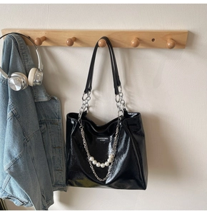 Detail of black glossy tote bag featuring silver chain and large white pearls decoration
